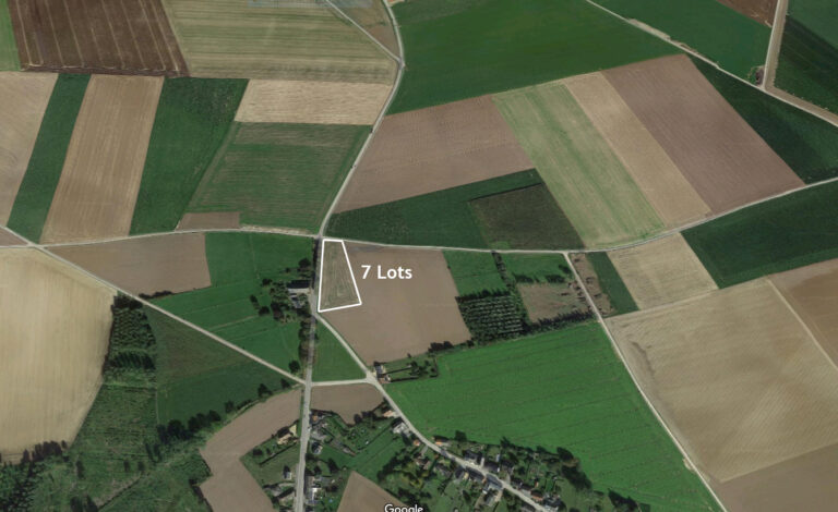 Vue aérienne d'un paysage rural de Taviers marqué des « 7 lots », mettant en valeur un patchwork de champs agricoles et de routes de couleurs variées.