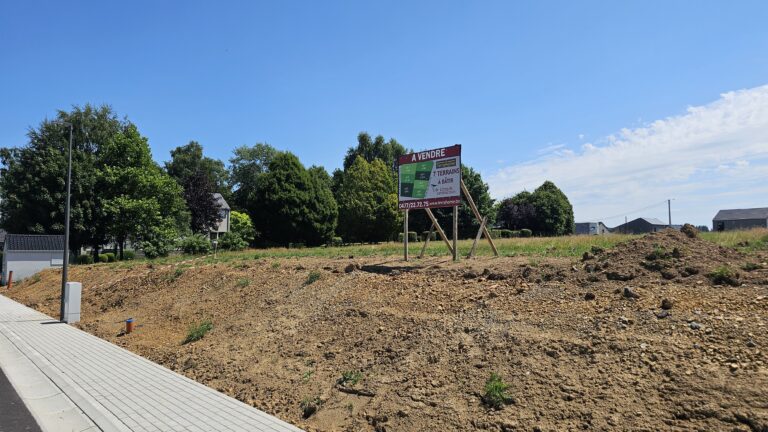 Un terrain vacant, légèrement surélevé, avec 4 façades et un panneau 
