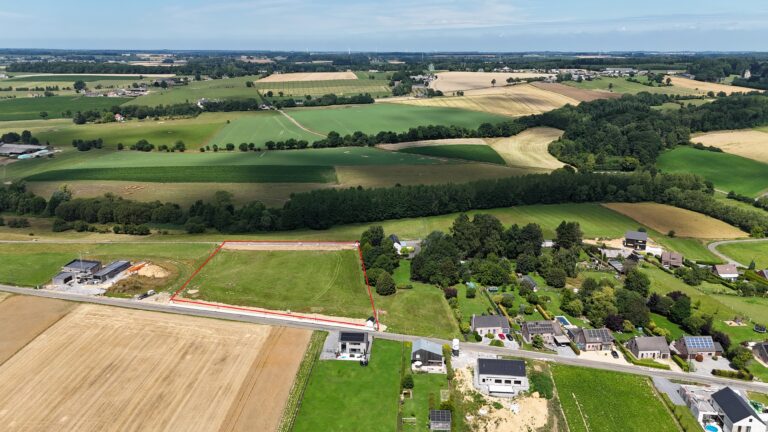 Vue aérienne d'un paysage rural dans le Hamois avec des champs verts, des maisons éparses avec 4 façades, des arbres et des terres agricoles qui s'étendent sur le terrain sous un ciel bleu.